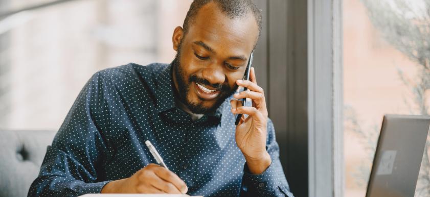 African American man working from home talking on phone and taking notes