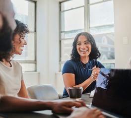 4 office workers sitting around a table looking at a laptop