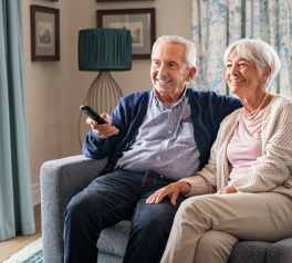 Two older adults sitting at home on couch with television remote